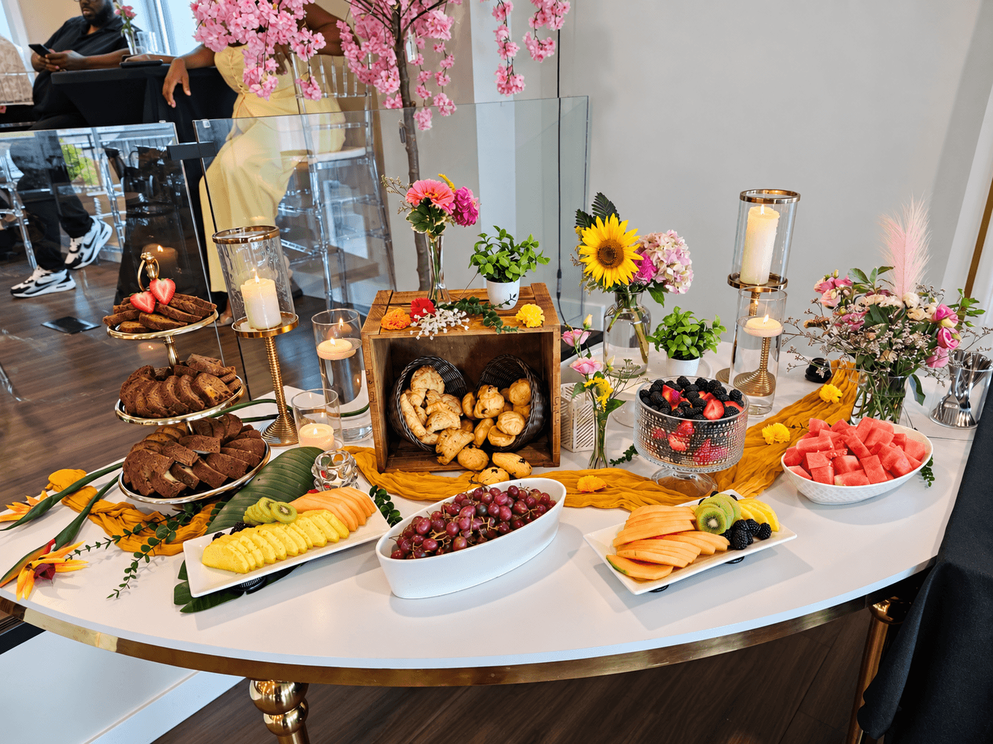 A catered grazing table with fresh fruit, flowers, and pastries